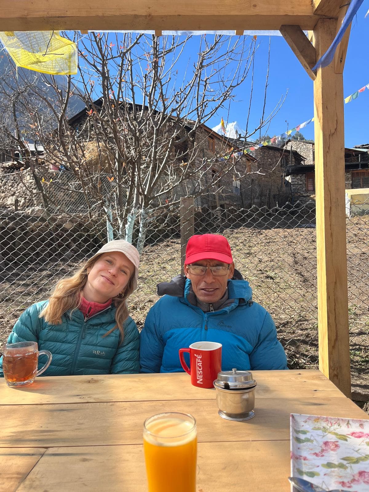 Smiling trekkers at a village tea house with a distant snowy Himalayan peak