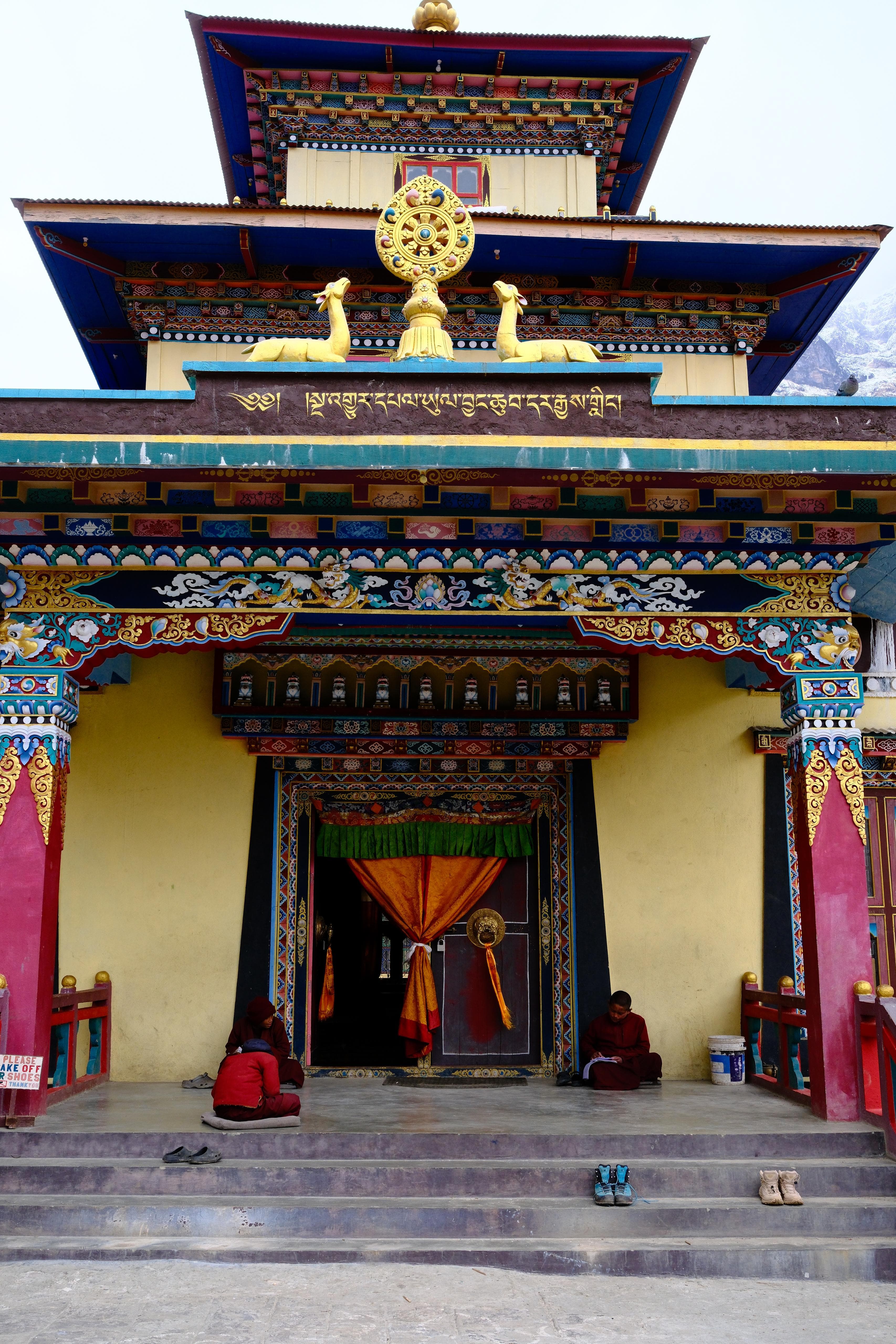 Vibrant Himalayan monastery with monks, trekking boots, and distant snowy mountain