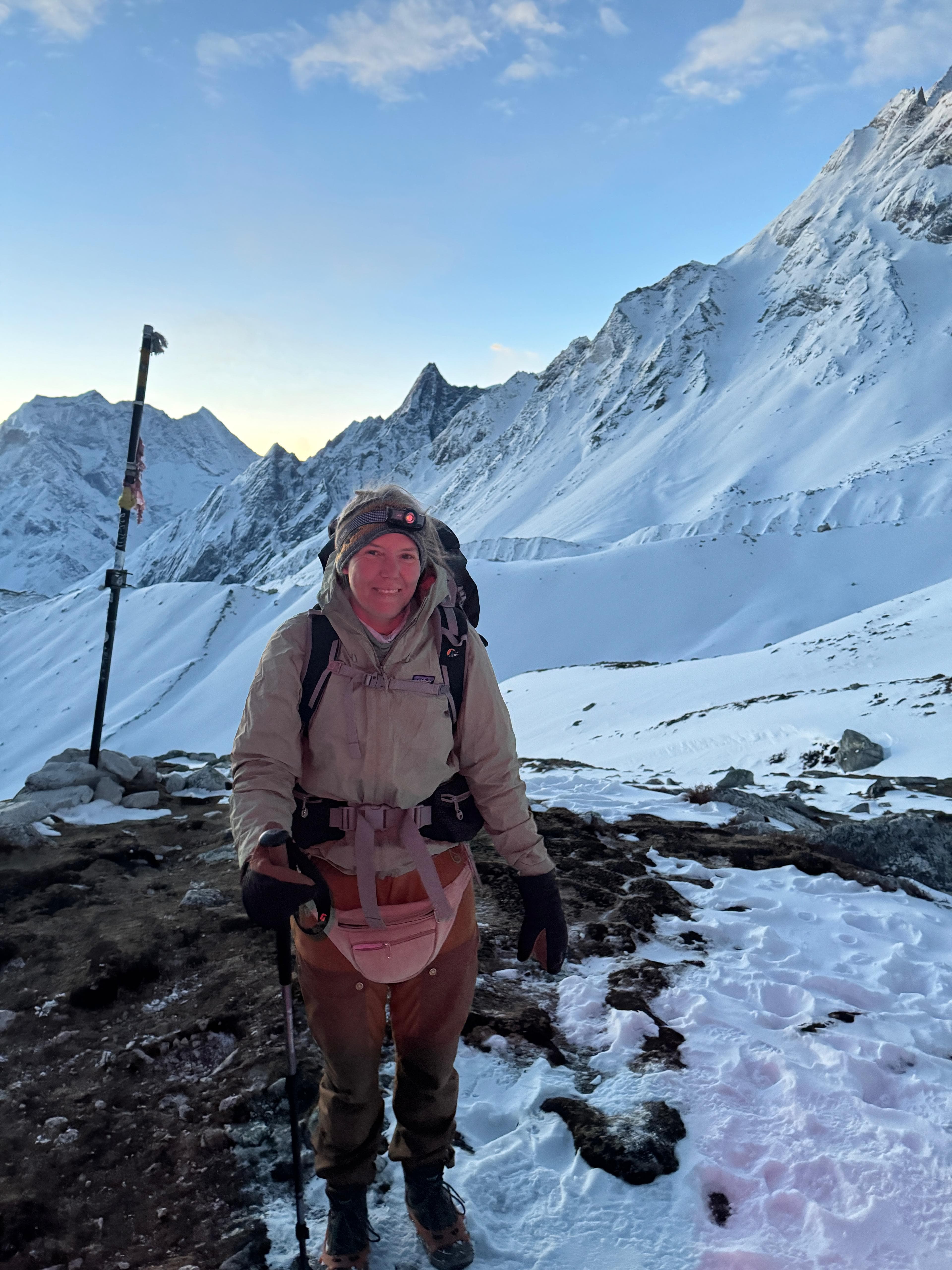 Smiling woman trekking a snowy Himalayan trail at sunrise with headlamp on