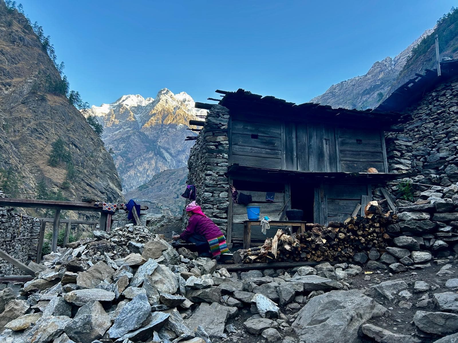 Local woman outside a traditional stone house against towering Himalayan peaks