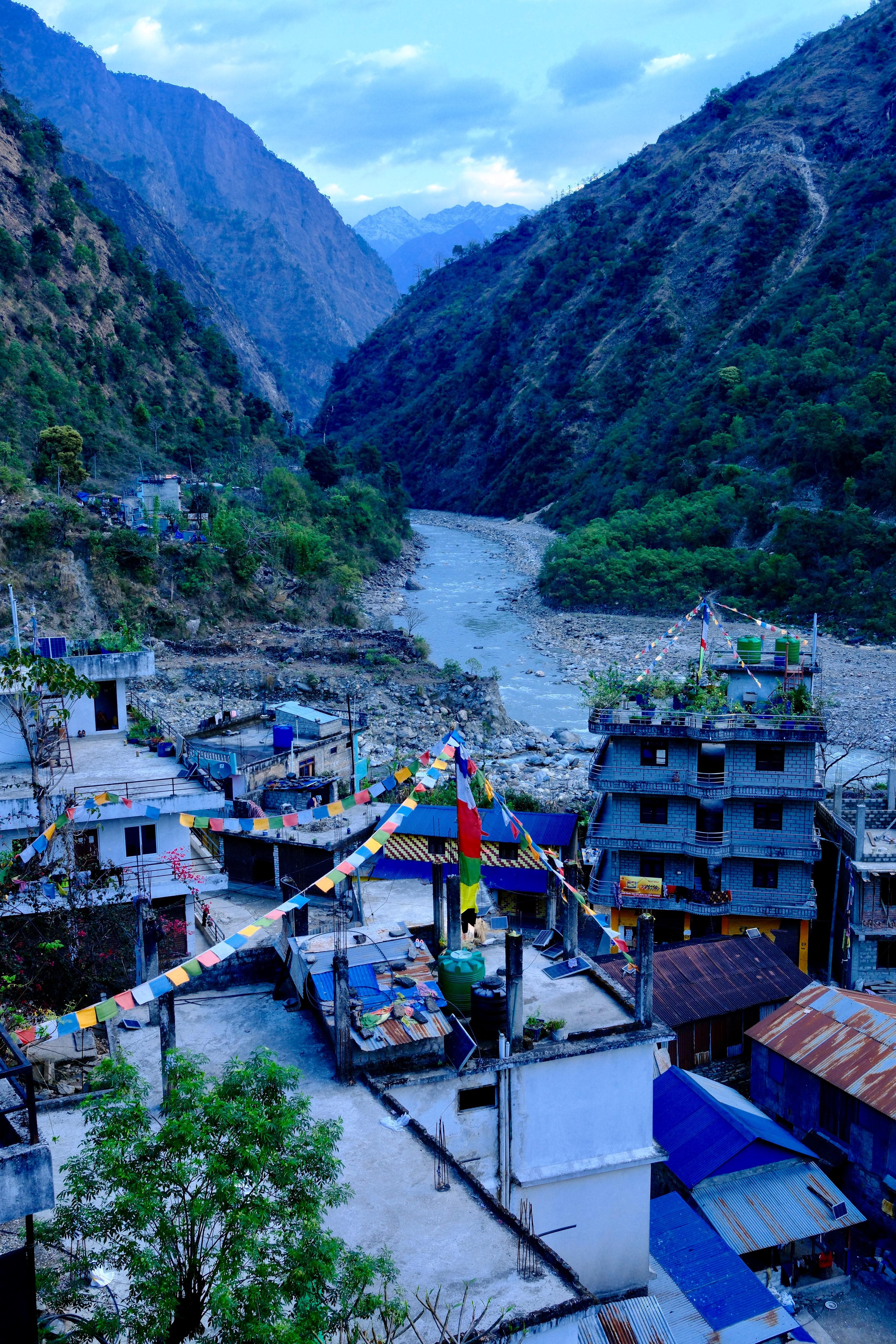 Nepali mountain village in deep valley with river, prayer flags, and distant Himalayas