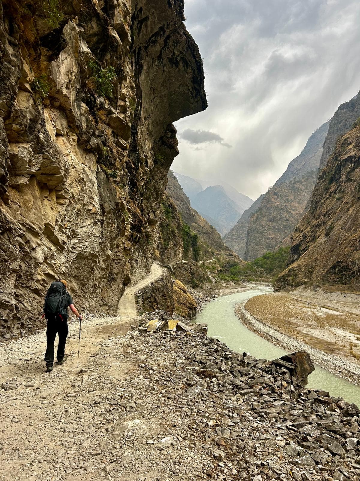 Trekker on a narrow cliffside trail above a river in a Himalayan valley