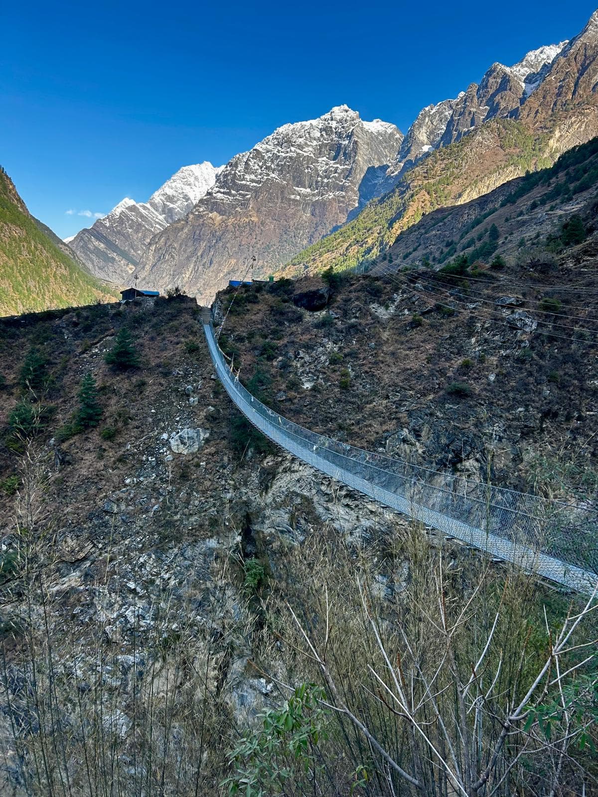 Long suspension bridge over a gorge with small settlement and snowy mountains