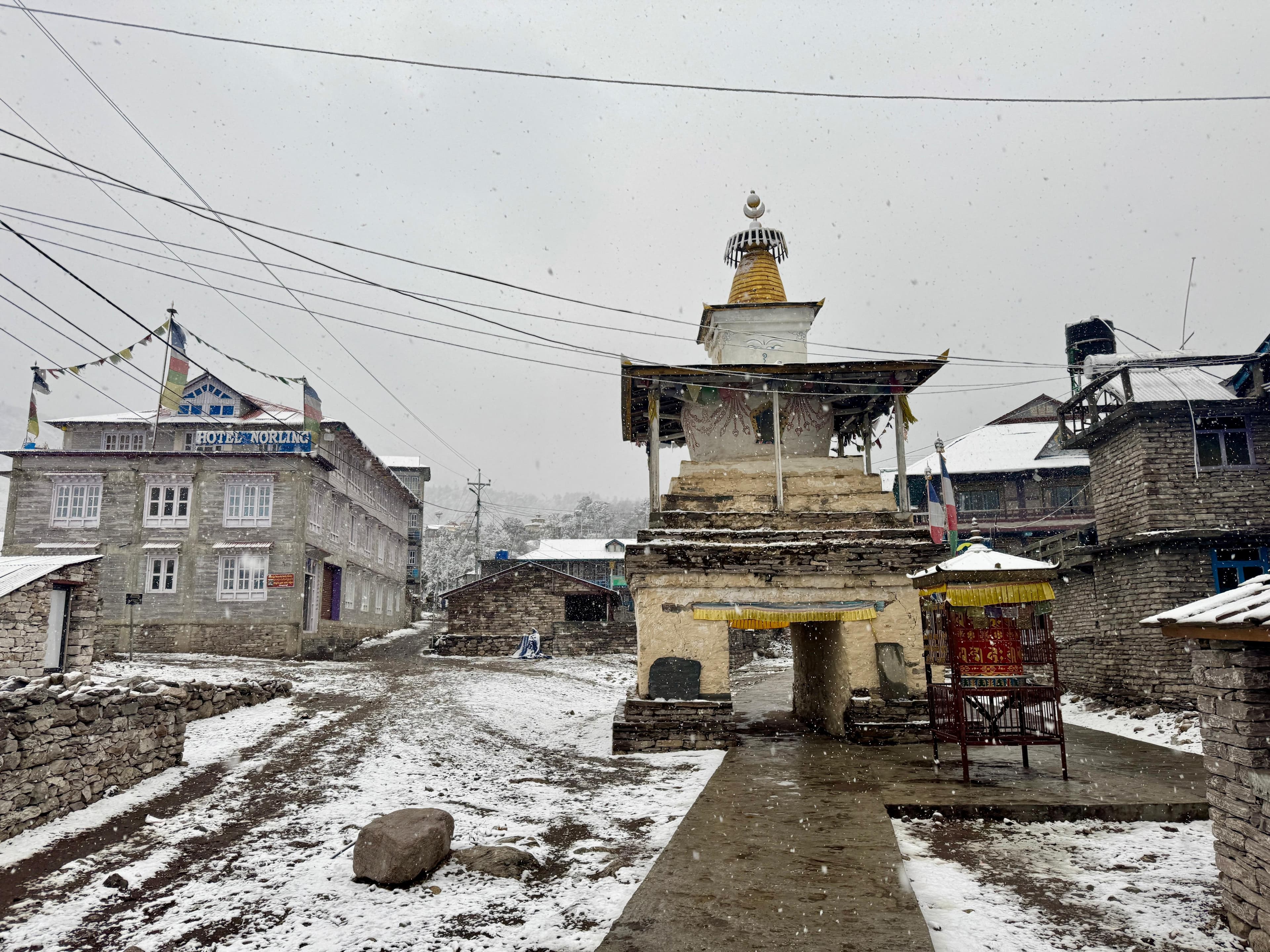 Snowy Himalayan village with a chorten, prayer flags, and trail