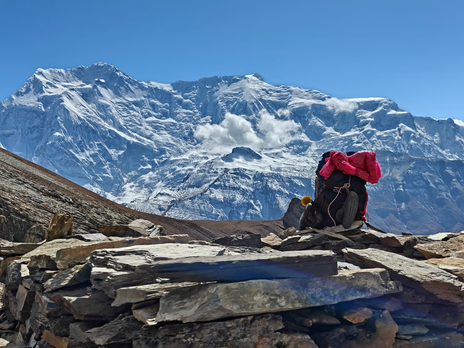 Snow-capped Annapurna mountain overlooks a trekking backpack on a rocky high-altitude path
