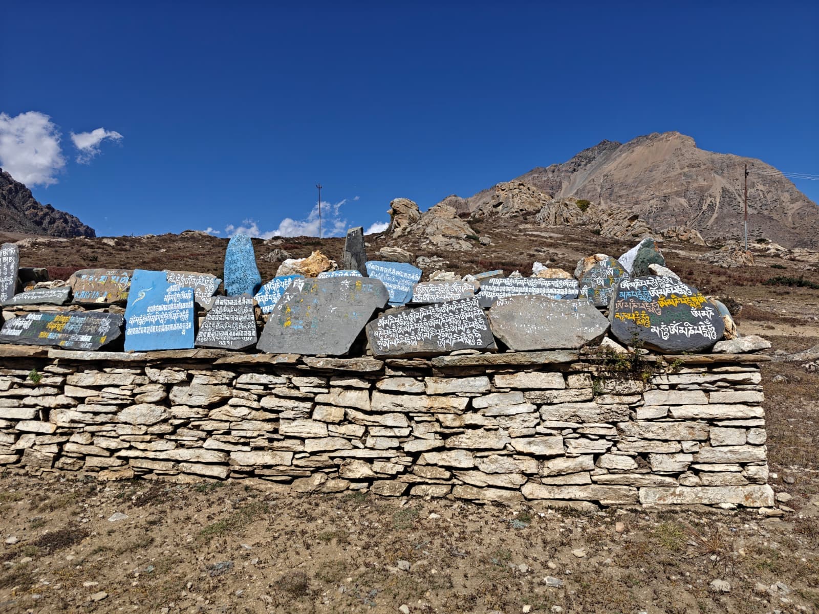 Tibetan mani wall with painted stones and rugged mountains under clear blue sky