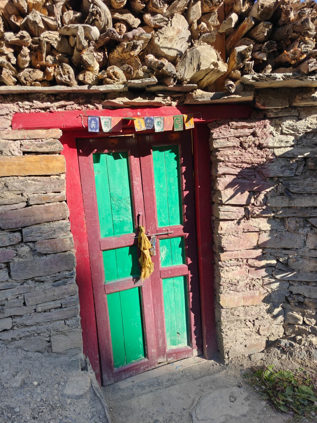 Colorful green door, prayer flags, and stacked wood on a stone Himalayan house