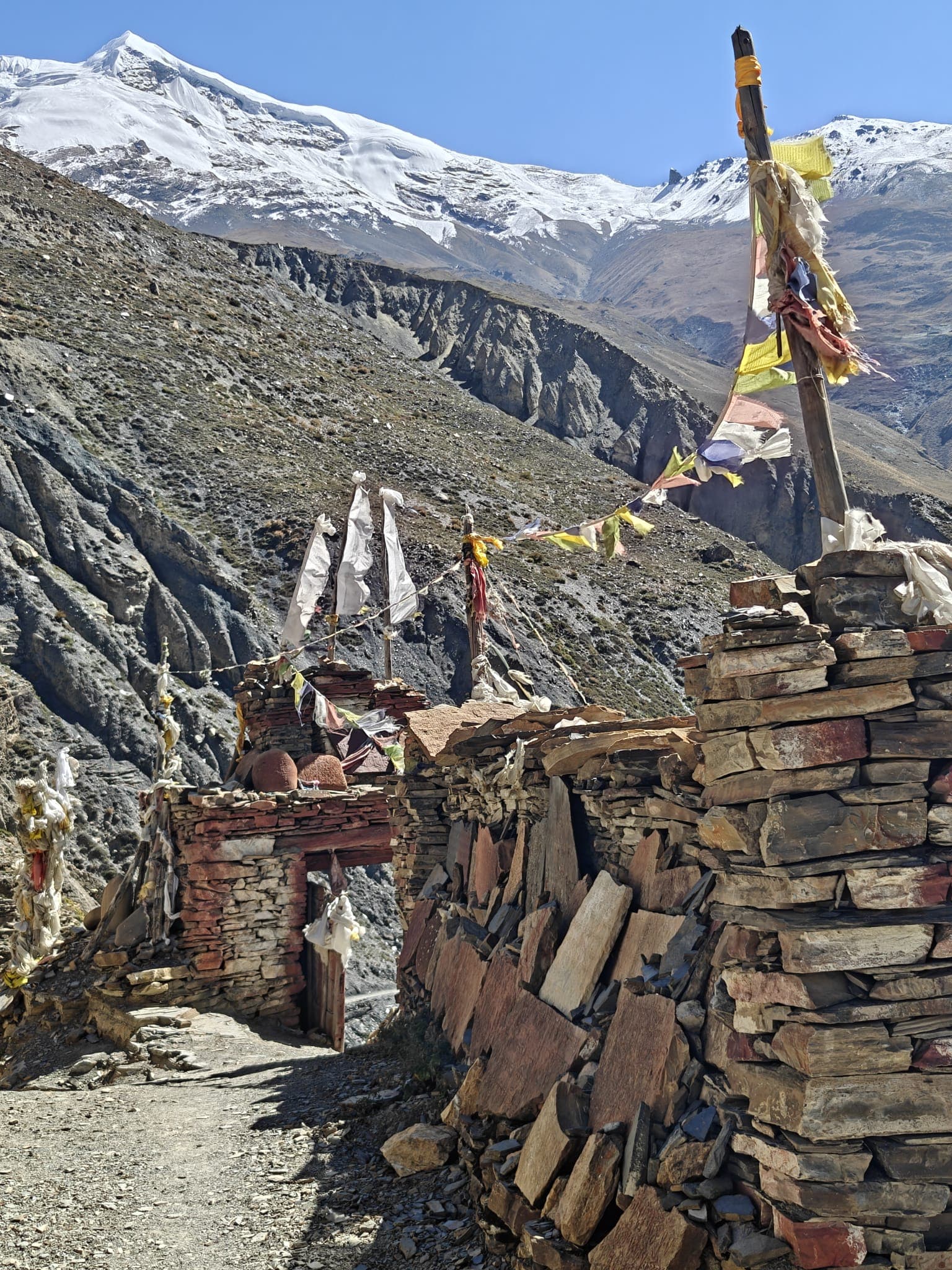 Himalayan trekking path with stone gate, prayer flags, and snow-capped peaks
