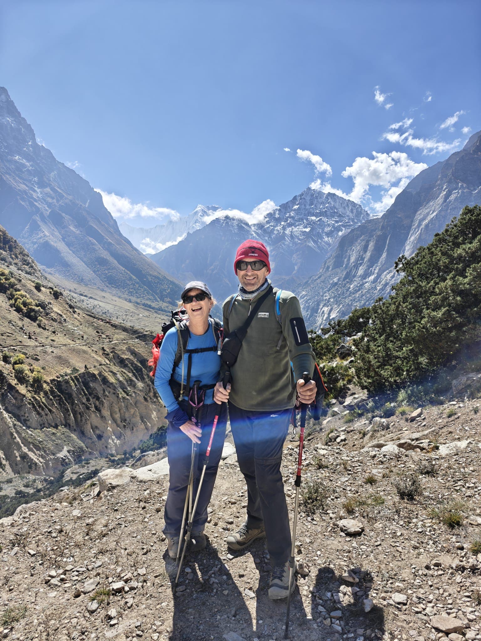 Smiling trekkers with poles on a rugged trail with towering Himalayan peaks