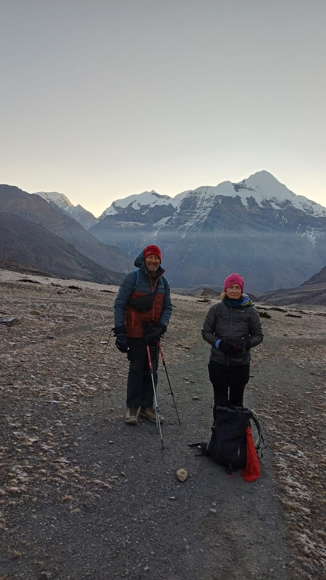 Two trekkers on a frosty, rugged trail below snow-capped Himalayan peaks