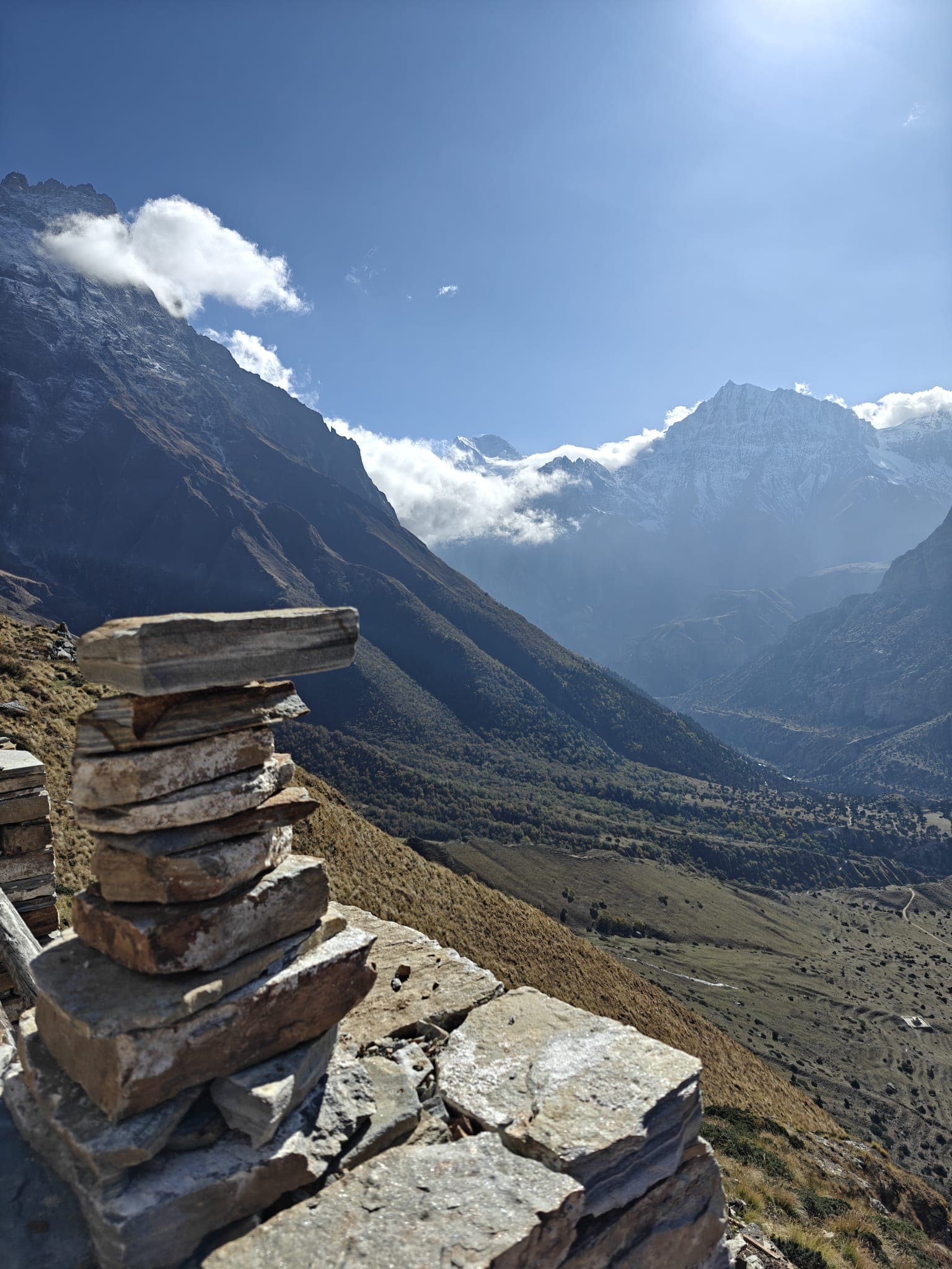 Stacked rocks overlook a vast Himalayan valley with towering snowy mountains
